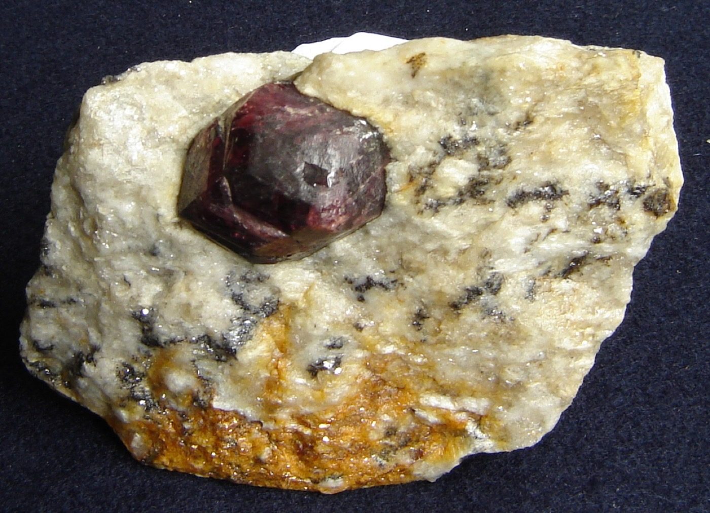 Raw dodecahedral almandine garnet crystal embedded in light-colored matrix rock